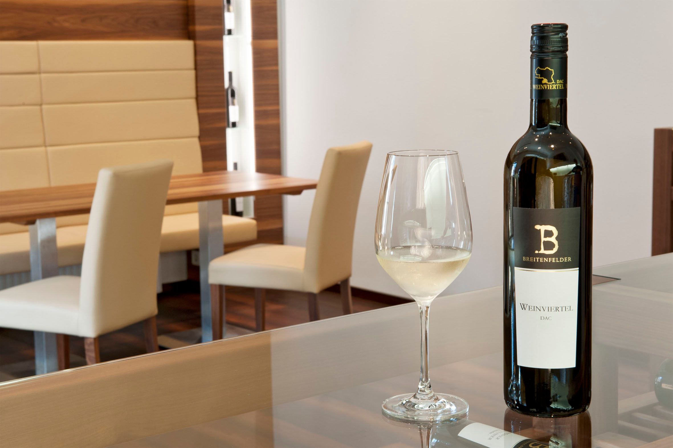 A tasting room with a bottle of white wine and a filled wine glass on a table.