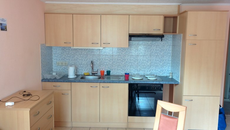 Small kitchen with wooden cupboards, sink, stove and tiled splashback.