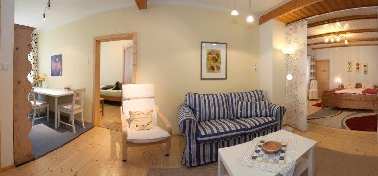 Panorama of a cozy living room with sofa, dining table and bedroom in the background.