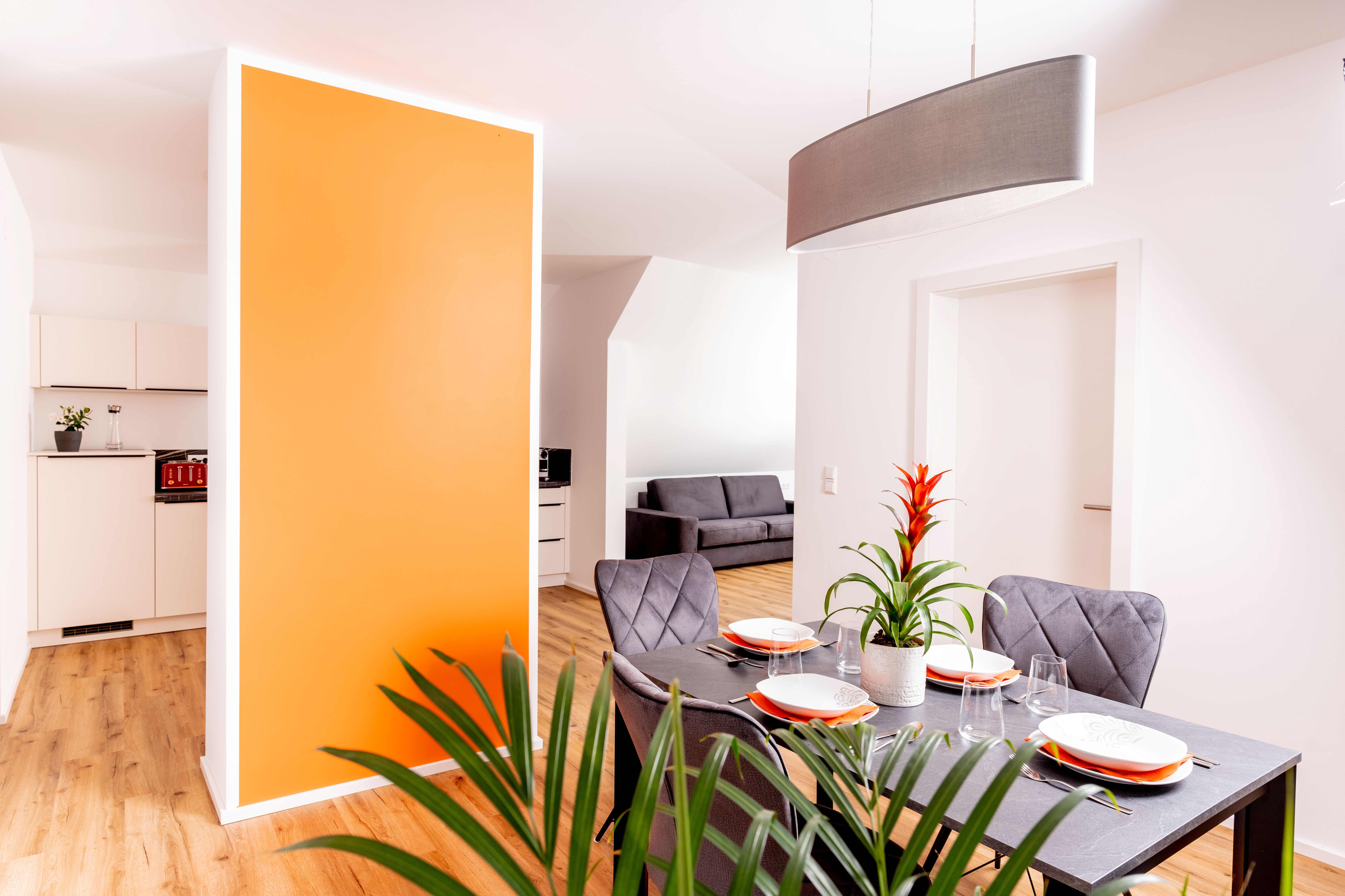 Modern apartment with dining area, orange wall and gray sofa.