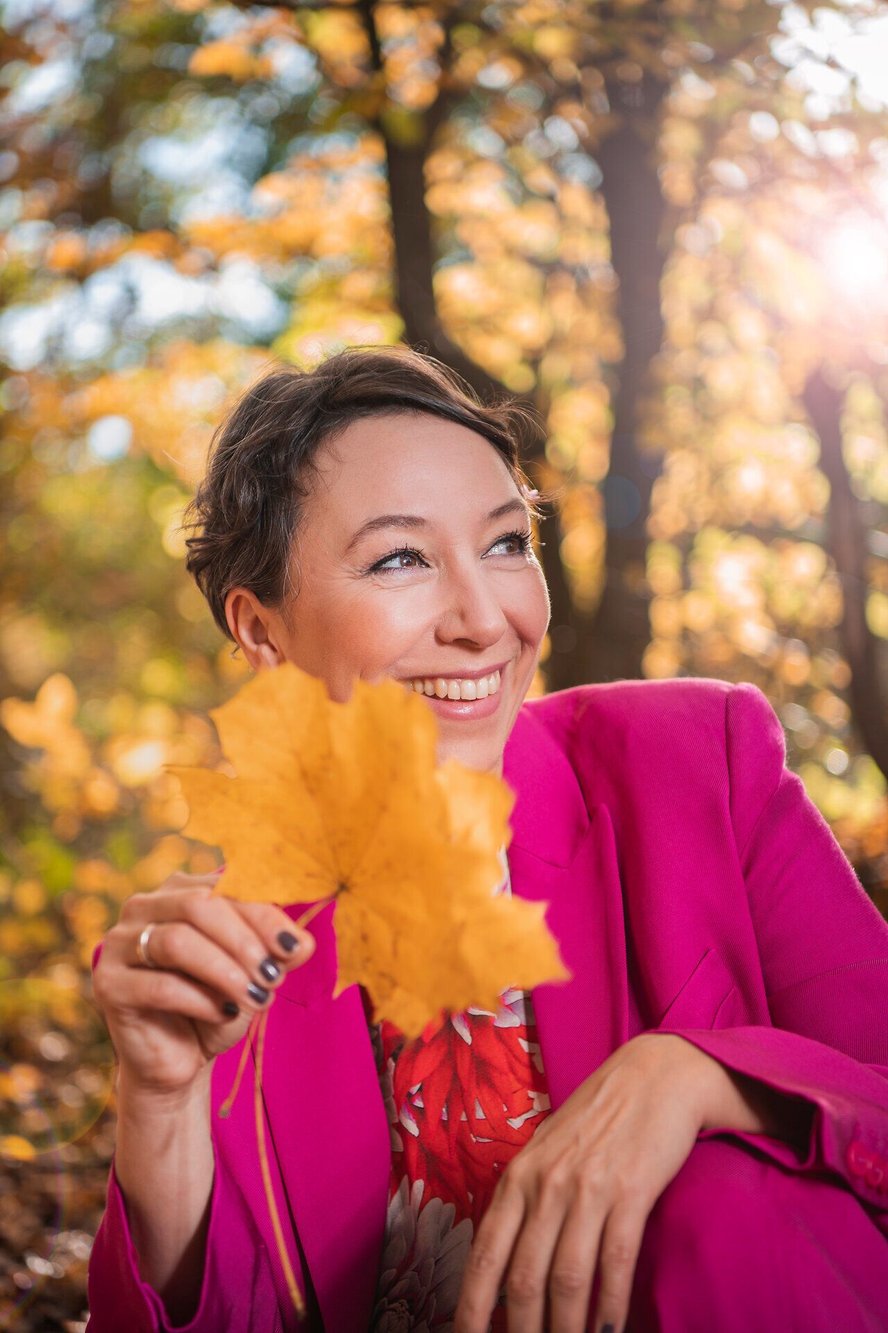 Porträt von Ursula Strauss, Künstlerische Leitung von Wachau in Echtzeit; lächelnd im herbstlichen Wald an der Donau in Niederösterreich, mit einem gelben Herbstblatt in der Hand.