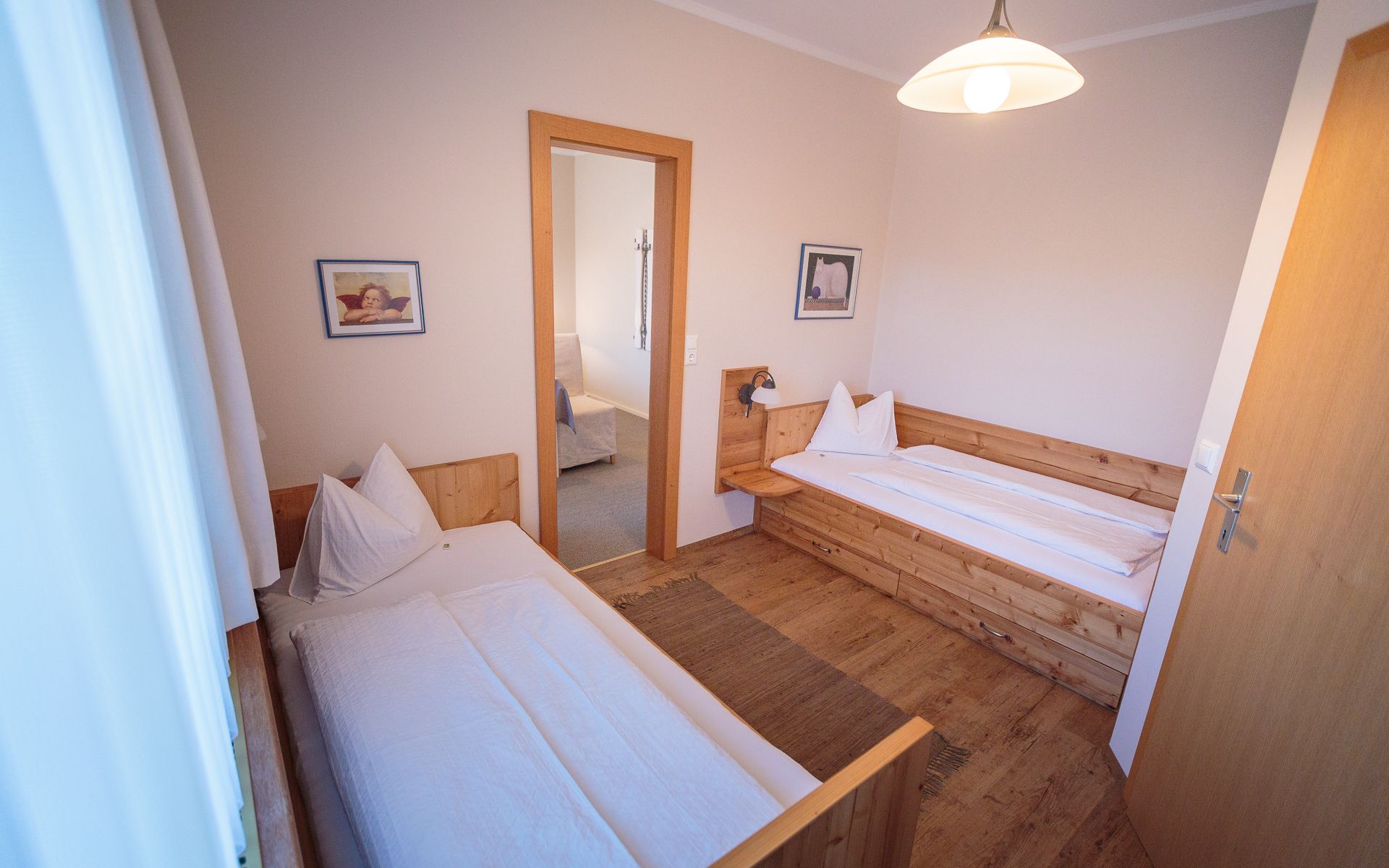 Two single beds in a cozy room with wooden furniture and pictures on the walls.