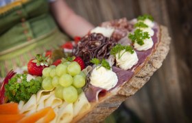A rustic platter with cheese, ham, grapes, strawberries and herbs.