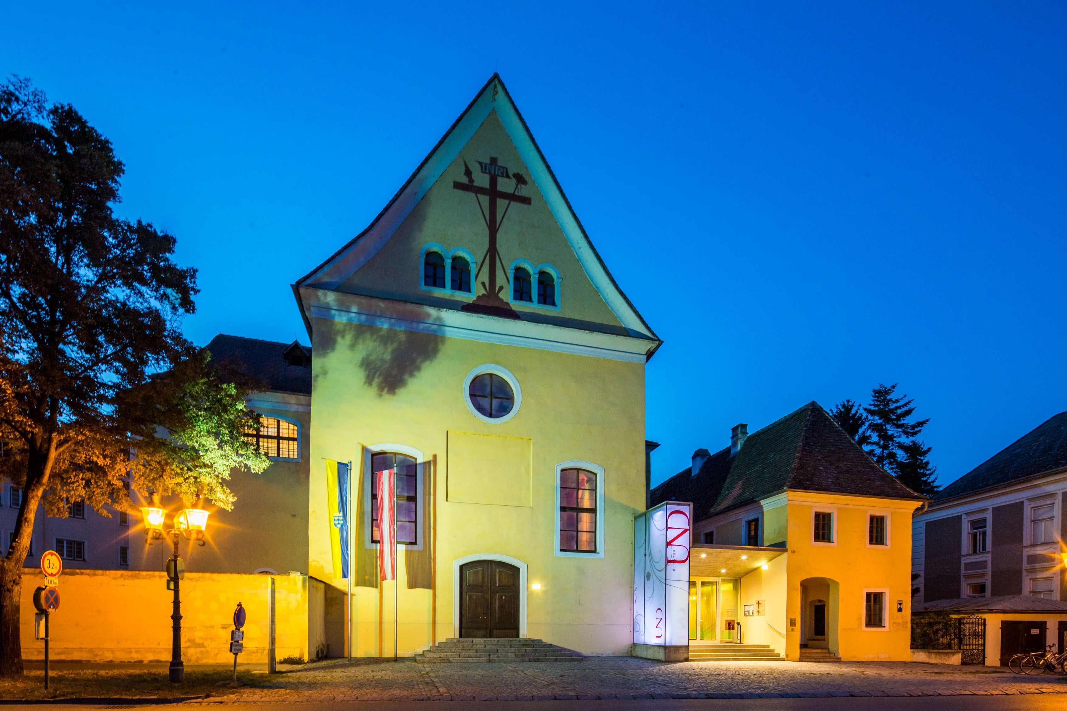 Yellow building with cross symbol, illuminated at night.