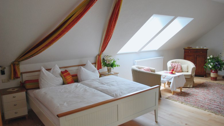 Cozy bedroom with double bed, armchairs and table under a sloping roof.