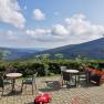Terrace with tables and chairs, view of green hills and blue sky with clouds.