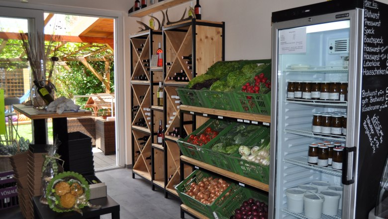 Interior view of a farm store with vegetables, wine shelves and refrigerator.