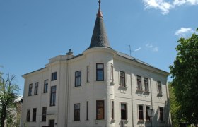 Historic building with tower and many windows, surrounded by trees.