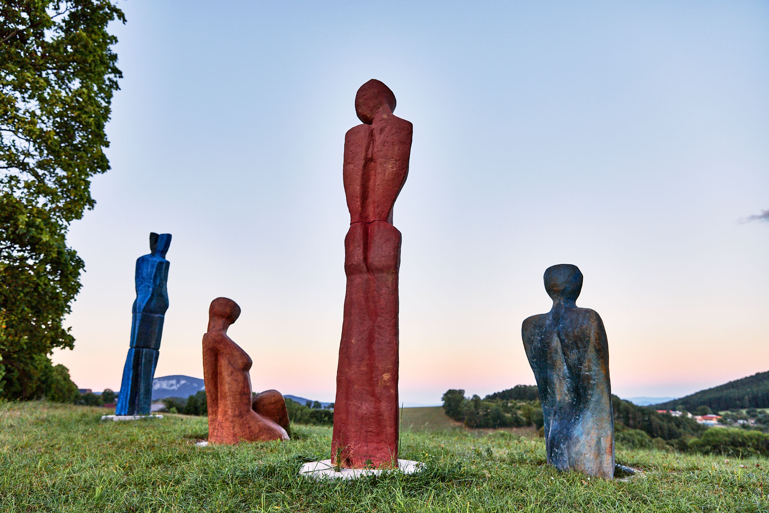 Four colorful sculptures on a meadow at sunset.
