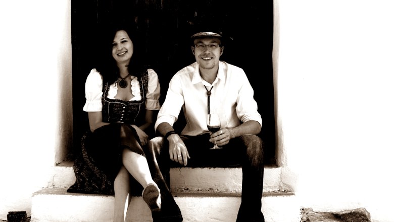 A man and a woman are sitting on a staircase, the man is holding a wine glass.