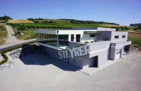 Modern Steyrer winery with glass façade and surrounding vineyards.