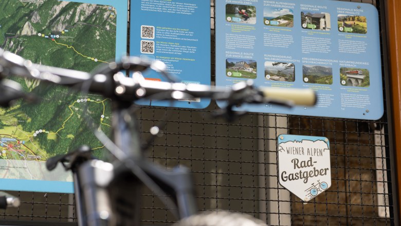 A bicycle stands in front of an information board with hiking and cycling trails in the Vienna Alps.