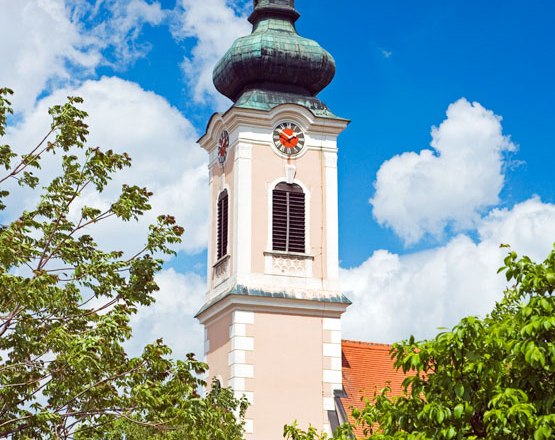 Tower of a church with clock and green roof in front of a blue sky.