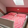 Bedroom with red wall, double bed with red bed linen, skylight and bedside table with wine bottle and glasses.