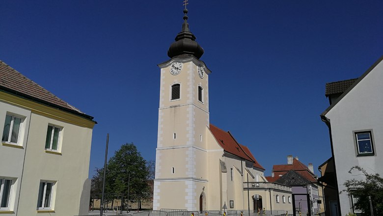 Church with tower and clock in Rohrendorf against a blue sky.
