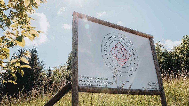 A sign for the Hatha Yoga Institute stands on a meadow under a sunny sky.