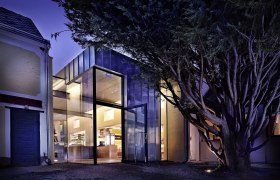 Modern glass facade of a building at night, surrounded by trees.