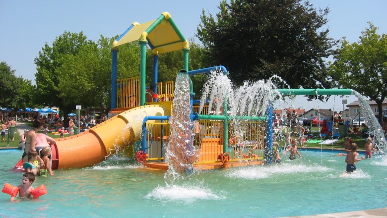 Children play in a water play garden with slides and water fountains.