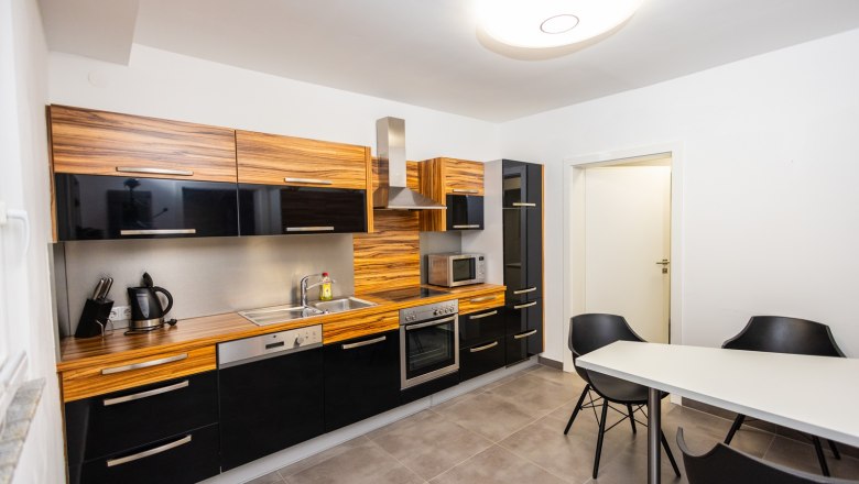 Modern kitchen with wooden and black elements, table and chairs.