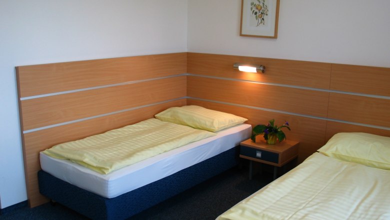 A simple hotel room with two single beds, a bedside table and a picture on the wall.