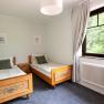 Bedroom with two single beds, wooden furniture and a large window with a view of the greenery.