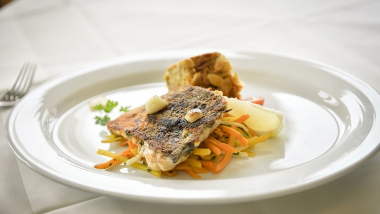A plate with fried fish fillet on vegetable strips and a side dish on a white tablecloth.