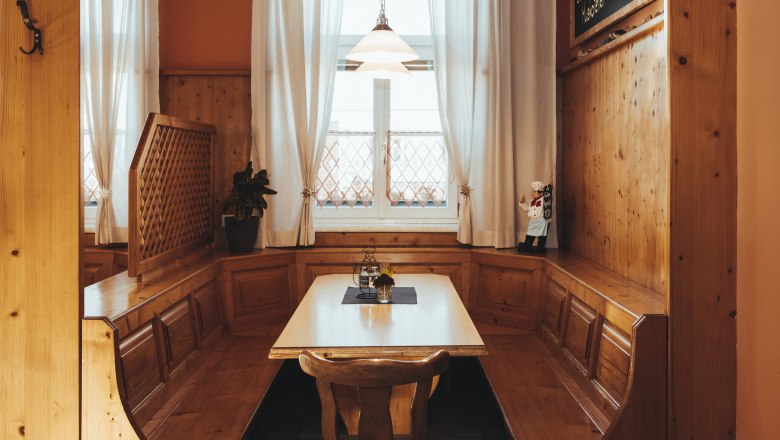 Cozy wooden corner bench with table in a rustic room, decorated with curtains and a small figure.