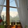 View of a mountain from a window with curtains. Two glasses of liquid are on the windowsill.