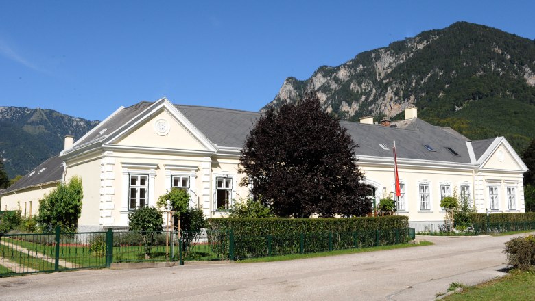 A large, bright building with a garden against a mountain backdrop.