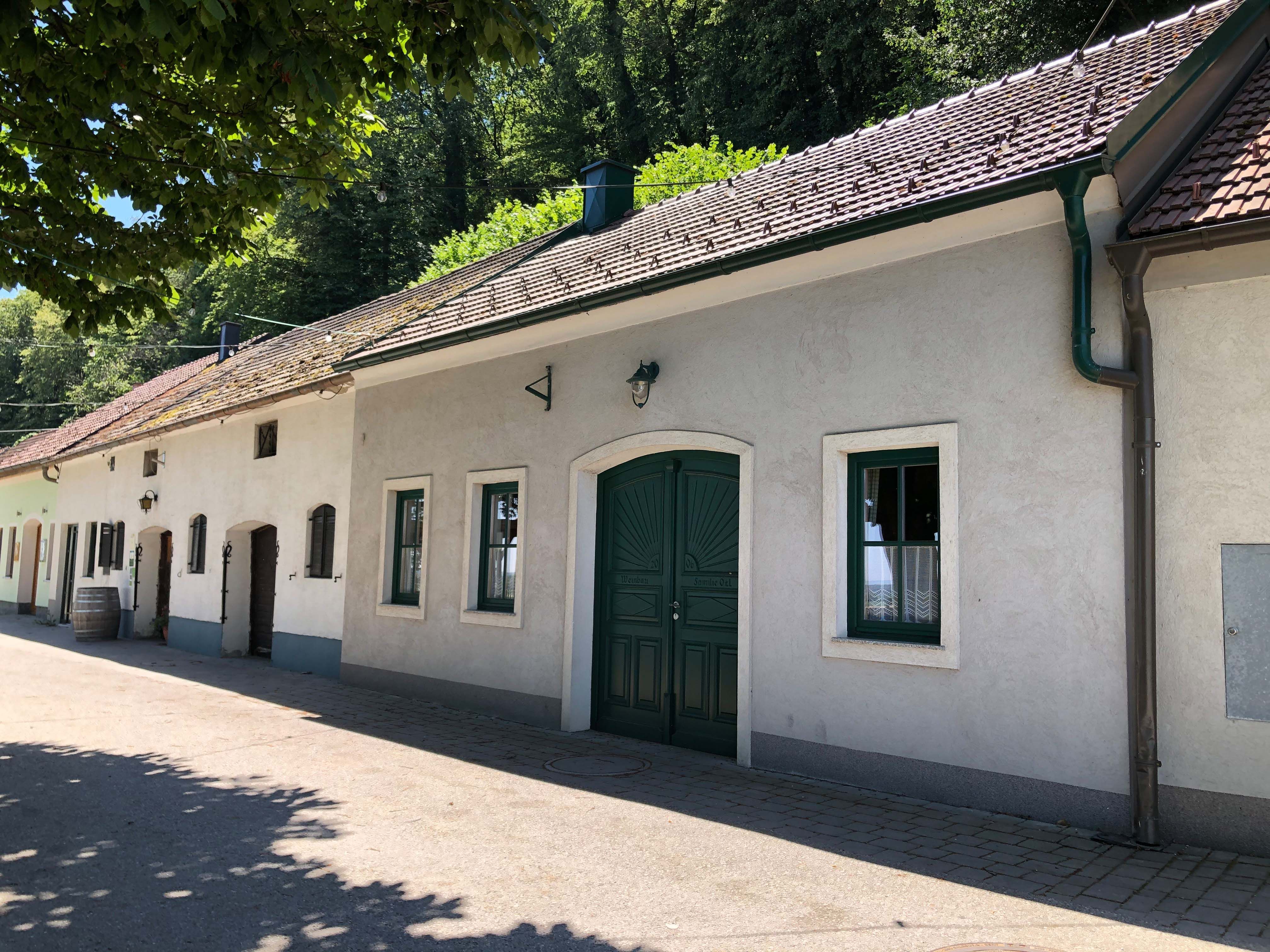 Exterior view of a traditional wine tavern with white walls and green gate, surrounded by trees.