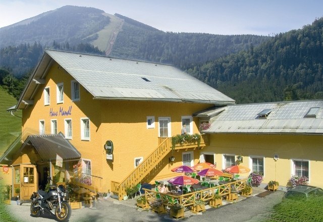 Yellow building with terrace and colorful parasols, surrounded by mountains.