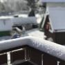 Snow-covered wooden beams in the foreground, blurred huts in the background.