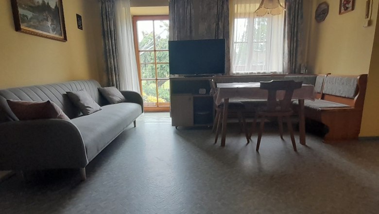 Kitchen-living room with sofa, dining table and TV in front of large windows.