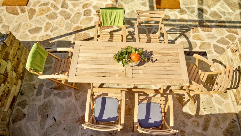 Wooden table with chairs on a stone terrace, decorated with pumpkins and flowers.