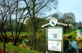 A river trail sign on a riverbank with bare trees in the background.