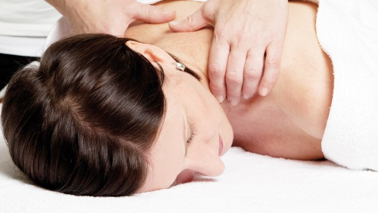 A woman receives a neck massage while lying on a white towel.
