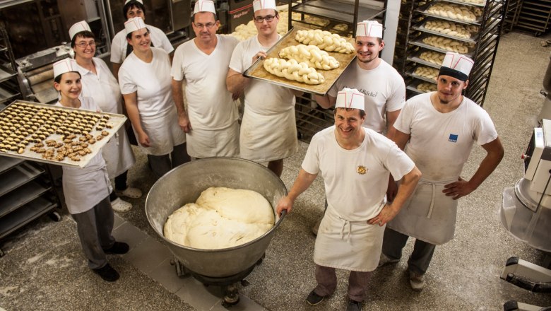 Employees of a bakery in white work clothes with trays full of pasta in a bakery.