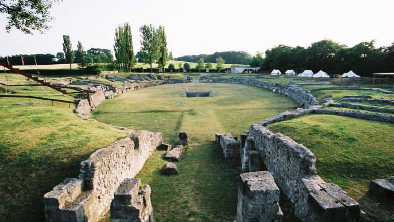 Ruins of an ancient amphitheater with a grassy interior and surrounding trees.