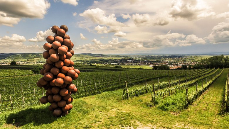 Sculpture of spheres in the shape of a bunch of grapes on a vineyard with a view of a landscape.