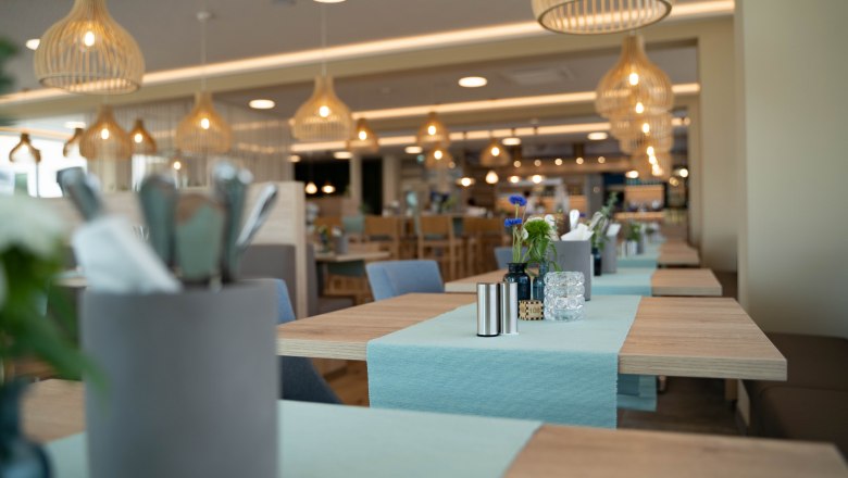 Interior view of a modern café with wooden tables, blue table runners and hanging lamps.