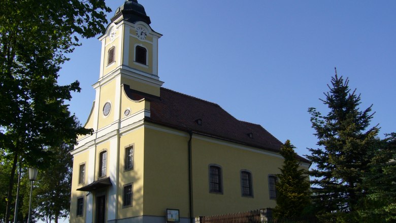 Haugschlag parish church with yellow fa&ccedil;ade and tower, surrounded by trees.