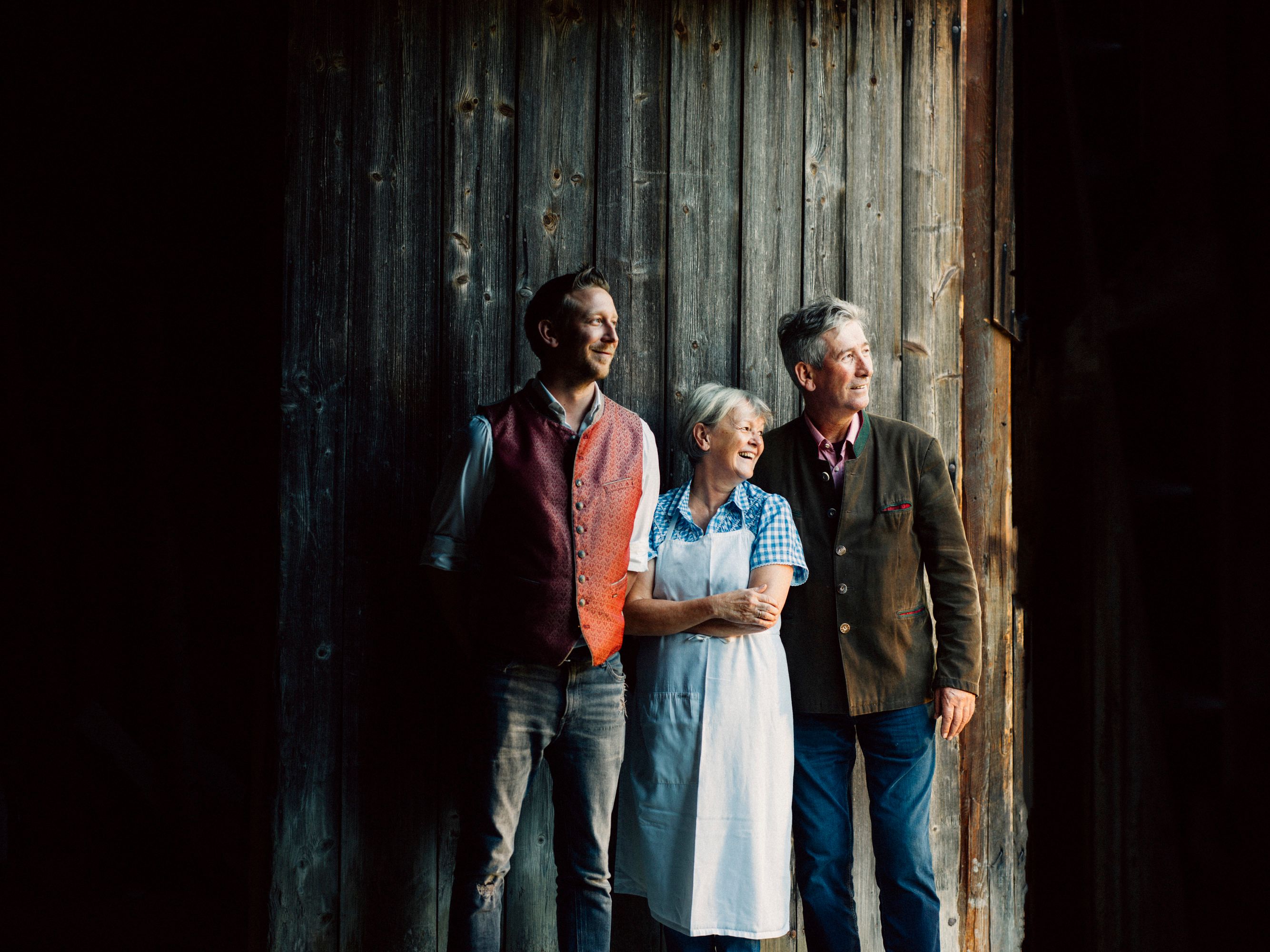 Three people stand smiling in front of a wooden wall and look to the right.