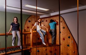 Children play in an indoor climbing area with wooden walls and colorful climbing holds.