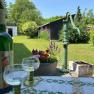 A green courtyard with an old water pump, flowers and a table with wine bottles and glasses.