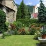 A well-tended monastery garden with blooming roses, a lawn and an old stone wall in the background.