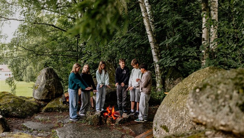 Group of young people standing around a campfire in the forest.