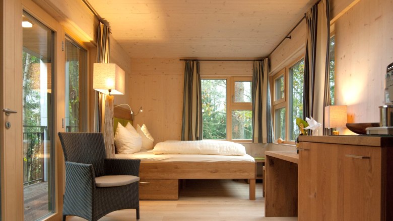 Interior view of a cozy tree house lodge with wooden furniture, bed, armchair and large skylight.