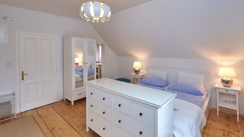 Bright bedroom with double bed, white closet and chest of drawers, wooden floor and modern ceiling lamp.