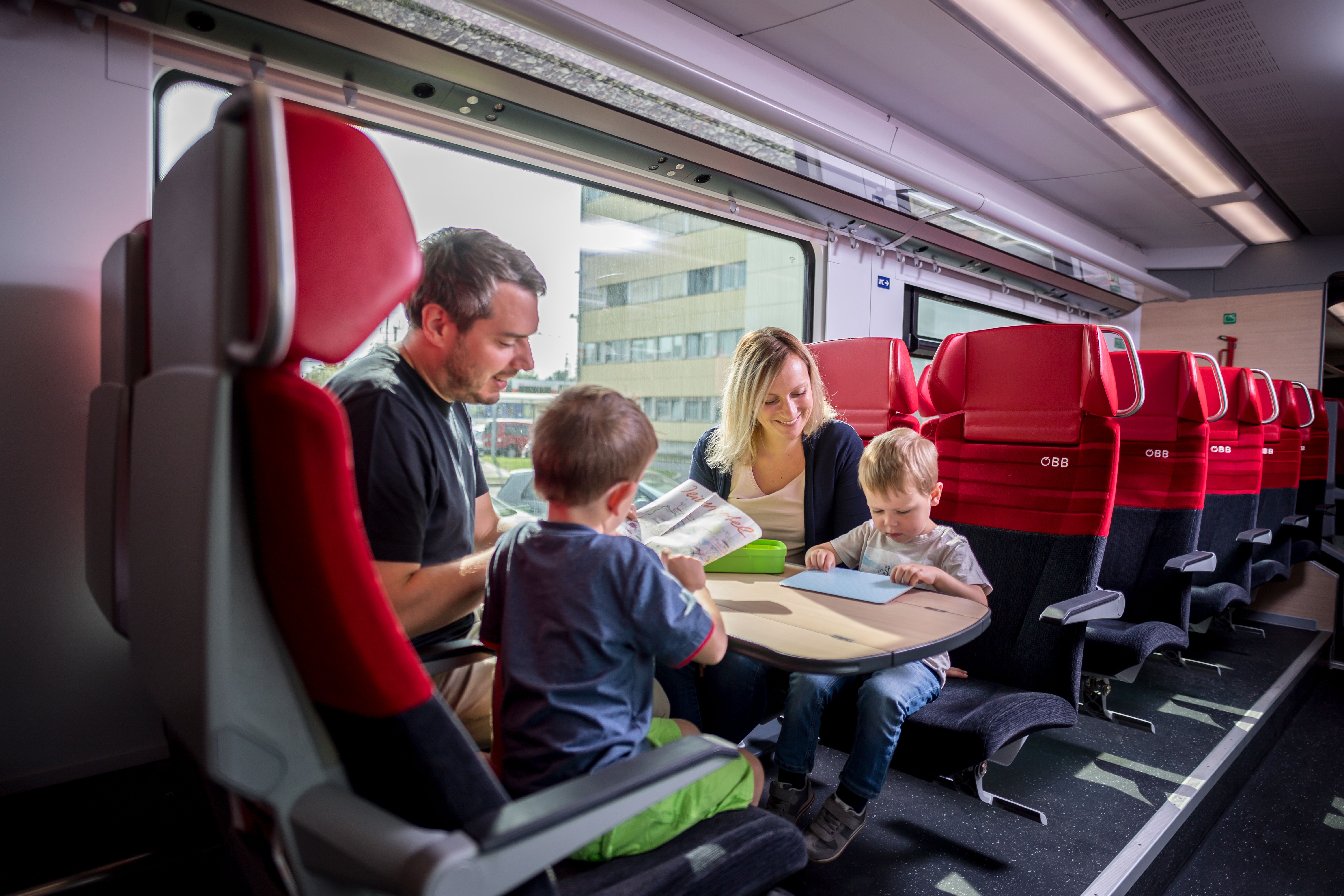 A family sits in an ÖBB train compartment and occupies itself with books and games.