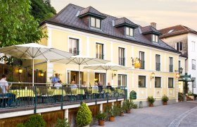 A yellow country inn with a terrace and parasols where people are sitting.